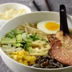 Jak zrobić ramen? Miska pełna aromatycznego bulionu z makaronem, plastrem boczku, jajkiem na pół, pak choi, kukurydzą i grzybami mun.