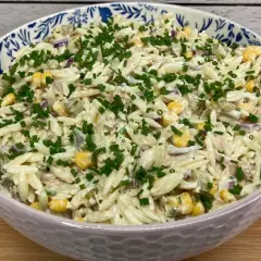 Pyszna sałatka z tuńczykiem i makaronem orzo, z kukurydzą i szczypiorkiem, podana w ozdobnej misce.