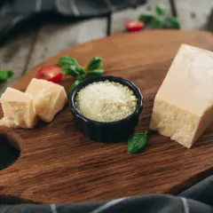 Kawałek parmezanu, pokrojony ser i starty ser do carbonary na drewnianej desce, ozdobione bazylią i pomidorkami.