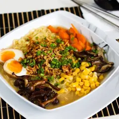 Miseczka aromatycznego tantanmen z makaronem, jajkiem na pół, kukurydzą, marchewką i grzybami shiitake, posypana szczypiorkiem.