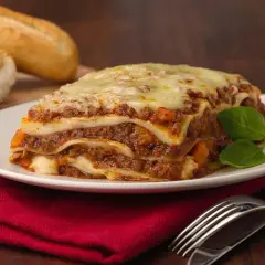 Pyszna, gorąca lasagne z mięsem i serem, idealna na obiad. Obok leżą świeże bagietki.