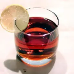 Szklanka z ciemnoczerwonym Martini Rosso, ozdobiona plasterkiem cytryny, stoi na jasnym blacie.