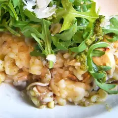 Kremowe risotto z pieczarkami, polane zielonym pesto i posypane parmezanem, z rukolą na wierzchu. Pyszne danie.