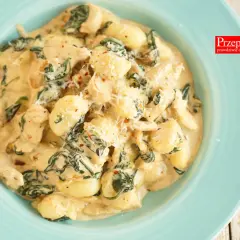Pyszne gnocchi z kurczakiem w sosie śmietanowym, ze szpinakiem i parmezanem, podane na turkusowym talerzu.