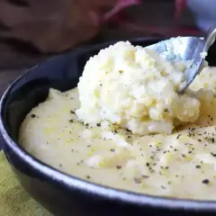 Łyżka nakłada kremową polentę z czarnym pieprzem z czarnej miski.