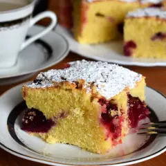 Szybkie ciasto bezglutenowe z wiśniami, posypane cukrem pudrem, na talerzyku obok filiżanki kawy.