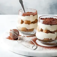 Dwa pucharki z deserem tiramisu, warstwy biszkoptów i kremu, posypane kakao. Idealna mizeria na słodko.