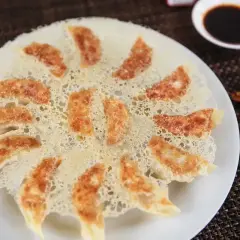 Chrupiące pierożki gyoza ułożone na talerzu, z chrupiącą panierką i sosem sojowym w tle.