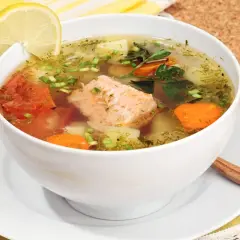 Aromatic rosyjska zupa rybna z łososiem, ziemniakami, marchewką i pomidorami, ozdobiona cytryną i koperkiem.
