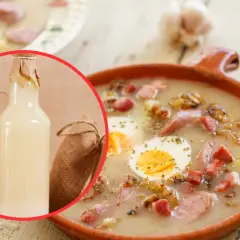 Aromaticzny żurek z białą kiełbasą i jajkiem, podany w glinianej misce. Obok buteleczka zakwasu, czosnek i chleb.