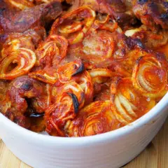 Pyszna karkówka pieczona w naczyniu z cebulą, duszona w sosie pomidorowym. Aromatyczne danie gotowe do podania.
