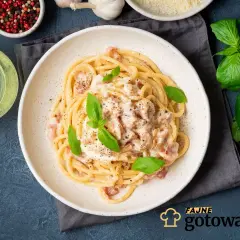 Pyszne spaghetti carbonara ze śmietaną bez jajek, udekorowane bazylią i pieprzem. Obok butelka oliwy i miseczka z pieprzem.