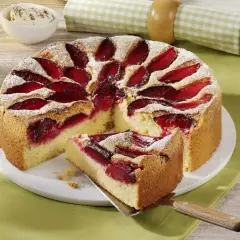 Puszyste ciasto ze śliwkami na oleju, posypane cukrem pudrem. Wygląda apetycznie i zachęca do spróbowania.