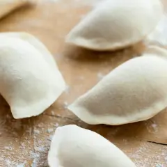 Surowe, niegotowe pierogi na drewnianej desce. To ciasto na pierogi bez jajka, gotowe do nadziewania.