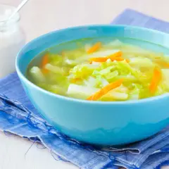 Aksamitna zupa z kalarepy z marchewką i kapustą, podana w błękitnej misce na niebieskiej serwetce. Obok słoiczek śmietany.