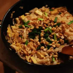 Pyszny sos pad thai z makaronem ryżowym, tofu, orzeszkami ziemnymi i szczypiorkiem, przygotowywany na patelni.
