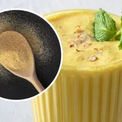 Pyszny, kremowy mango lassi w szklance, ozdobiony miętą i orzechami. Obok łyżka z proszkiem, być może przyprawa do mango lassi.