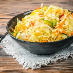 Kolorowa surówka z kiszonej kapusty inaczej, z dodatkiem marchewki, papryki i innych warzyw, podana w czarnej misce.