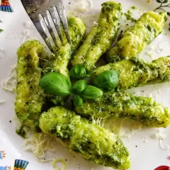 Pyszne gnocchi z pesto, posypane parmezanem i udekorowane listkami bazylii. Widok na talerzu z kolorowym wzorem.