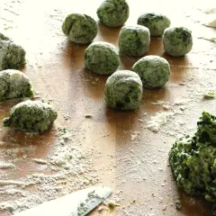 Zielone, domowe gnocchi ze szpinakiem, obtoczone mąką, czekają na ugotowanie.