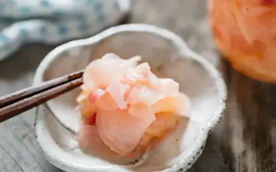 Różowy imbir do sushi, delikatnie podany na talerzyku z pałeczkami. Idealny dodatek do każdego sushi.
