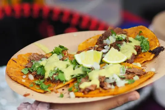 Talerz z trzema tacos w stylu tex mex, polanych zielonym sosem, posypanych kolendrą i cebulką, z ćwiartkami limonki.