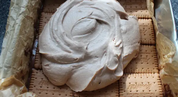 Ciasto Kinder Bueno z mascarpone w trakcie przygotowania. Kremowa masa rozpływa się na warstwie herbatników.