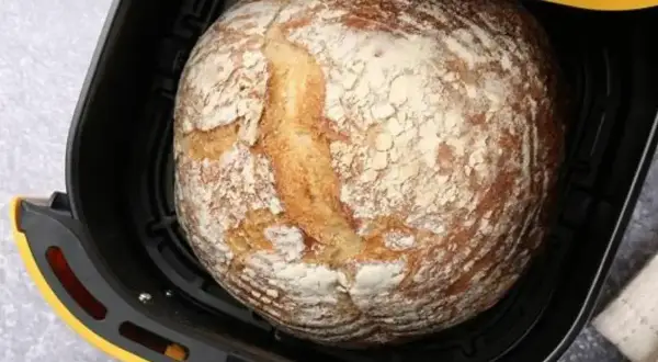 Chleb z airfryer, rumiany i lekko oprószony mąką, czeka na wyjęcie.