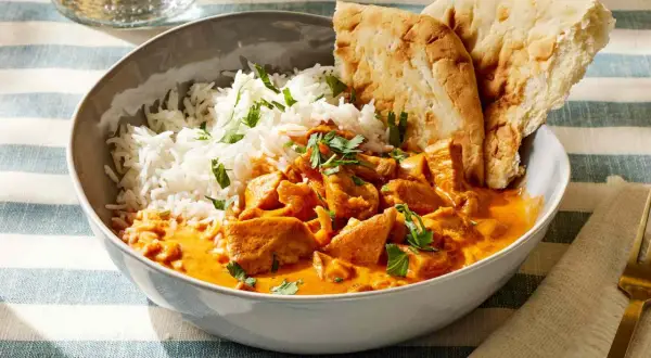 Miseczka z ryżem i kurczakiem w kremowym sosie butter masala, ozdobiona natką pietruszki, podana z chlebkiem naan.