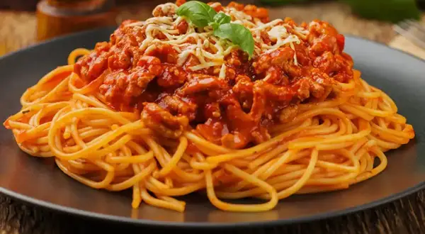 Pyszne spaghetti bolognese, idealne na prosty obiad. Makaron z bogatym sosem mięsnym, posypany serem i udekorowany bazylią.