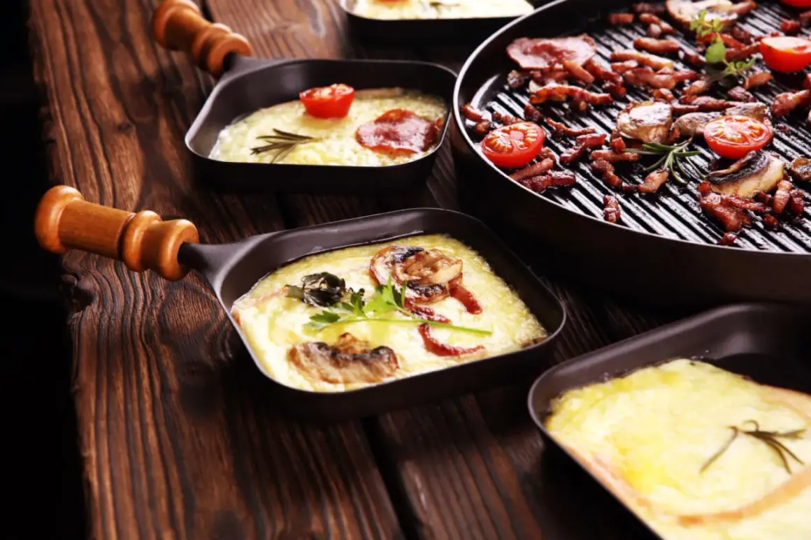Roztopiony ser raclette w małych patelenkach, z dodatkiem pomidorków i grzybów, obok grillowany boczek.