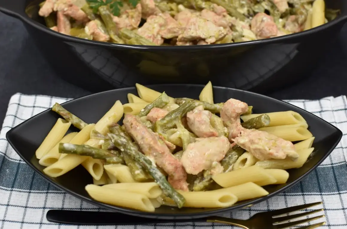 Penne z kurczakiem i szparagami w kremowym sosie. Pyszne danie na talerzu i w garnku.