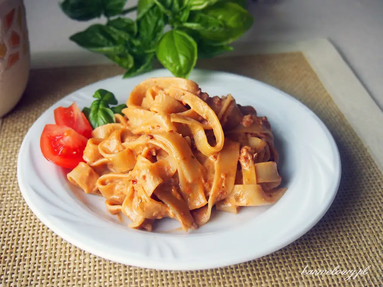 Pappardelle z kremowym, pomarańczowym sosem, który wygląda jak makaron z pesto ze słoika. Udekorowane pomidorkami i listkami bazylii.