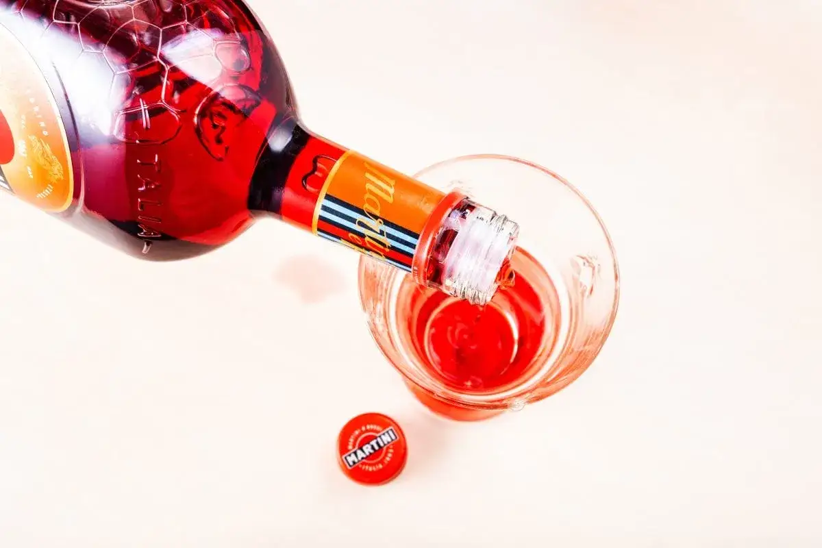 Czerwony Martini Rosso leje się z butelki do kieliszka. Obok leży zakrętka.