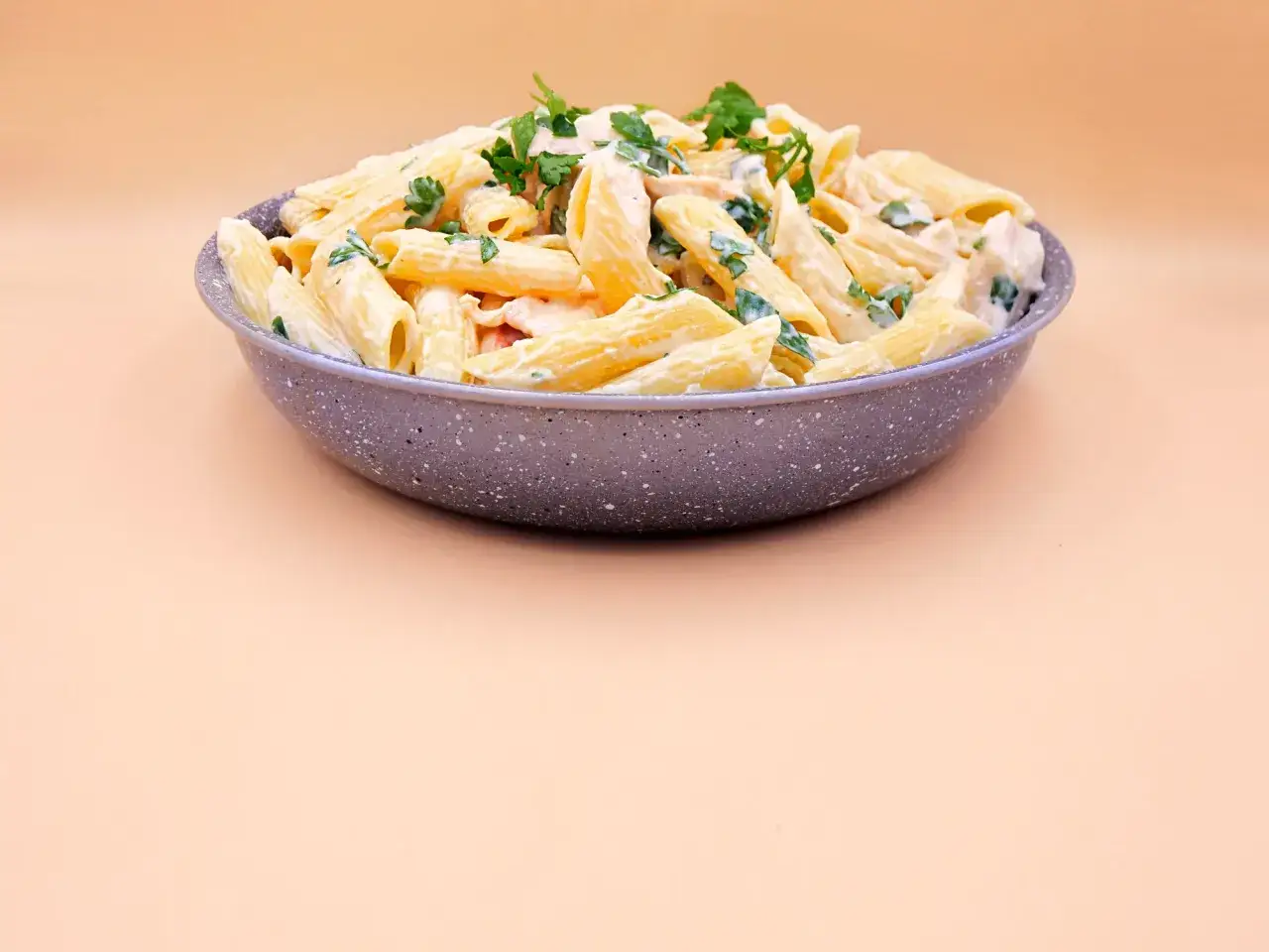 Penne z kurczakiem i szparagami w kremowym sosie, posypane natką pietruszki. Pyszne danie na obiad.