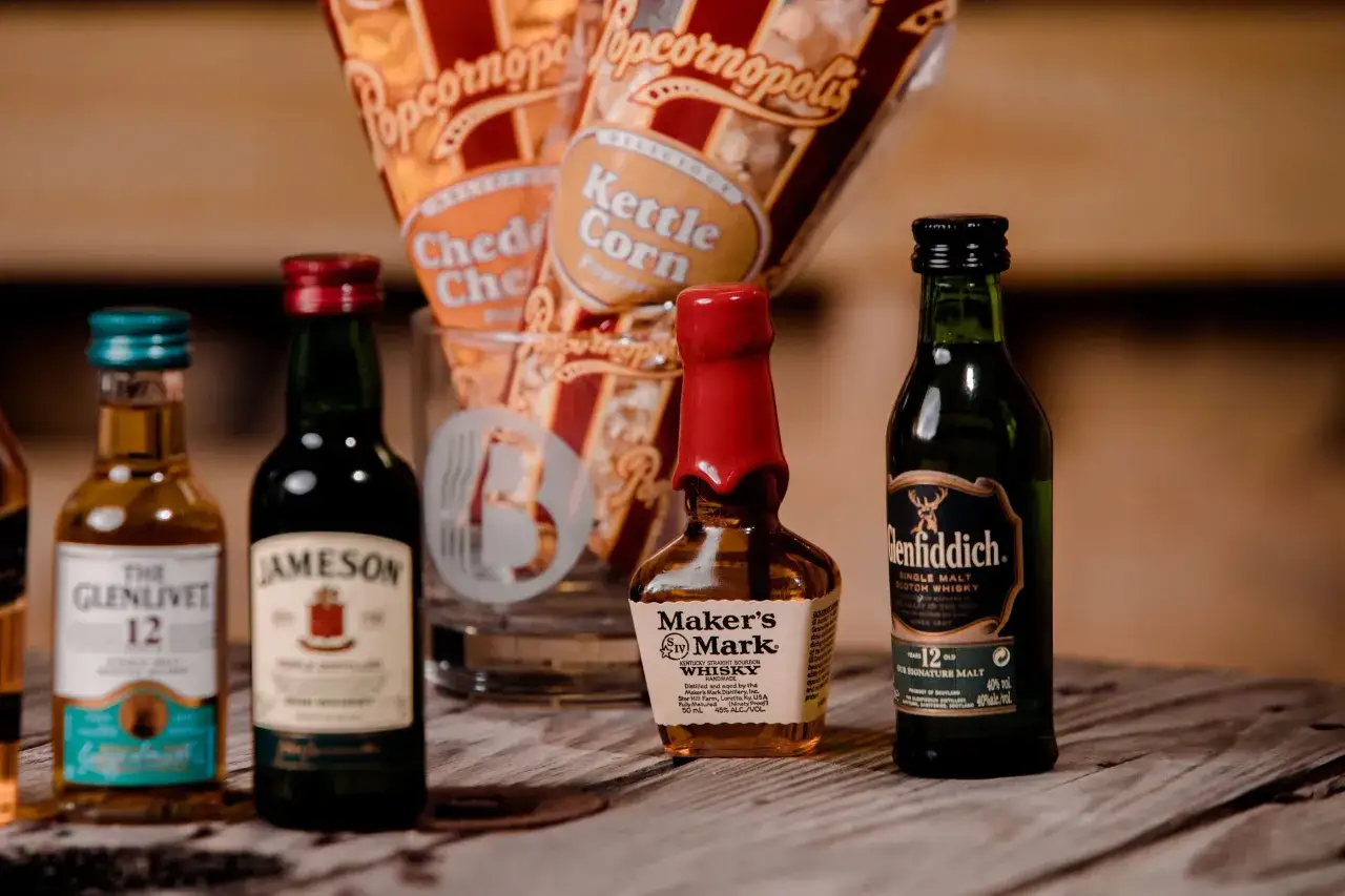 Miniaturki Glenlivet, Jameson, Maker's Mark i Glenfiddich – idealne na prezent dla konesera. Obok popcorn.