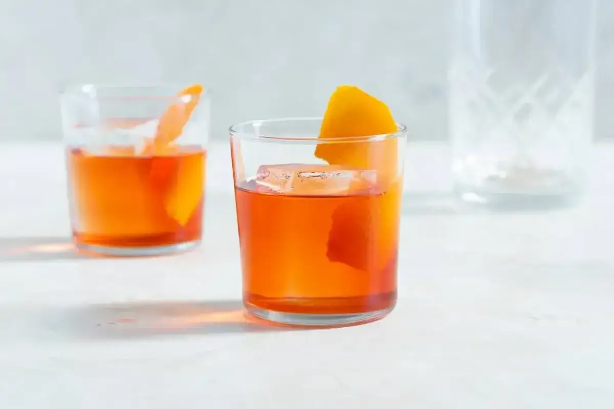 Klasyczny negroni przepis: dwa drinki z lodem i skórką pomarańczy na jasnym tle.