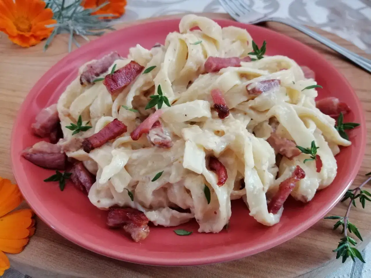 Pyszne tagliatelle z boczkiem i kremowym sosem, udekorowane świeżym tymiankiem.