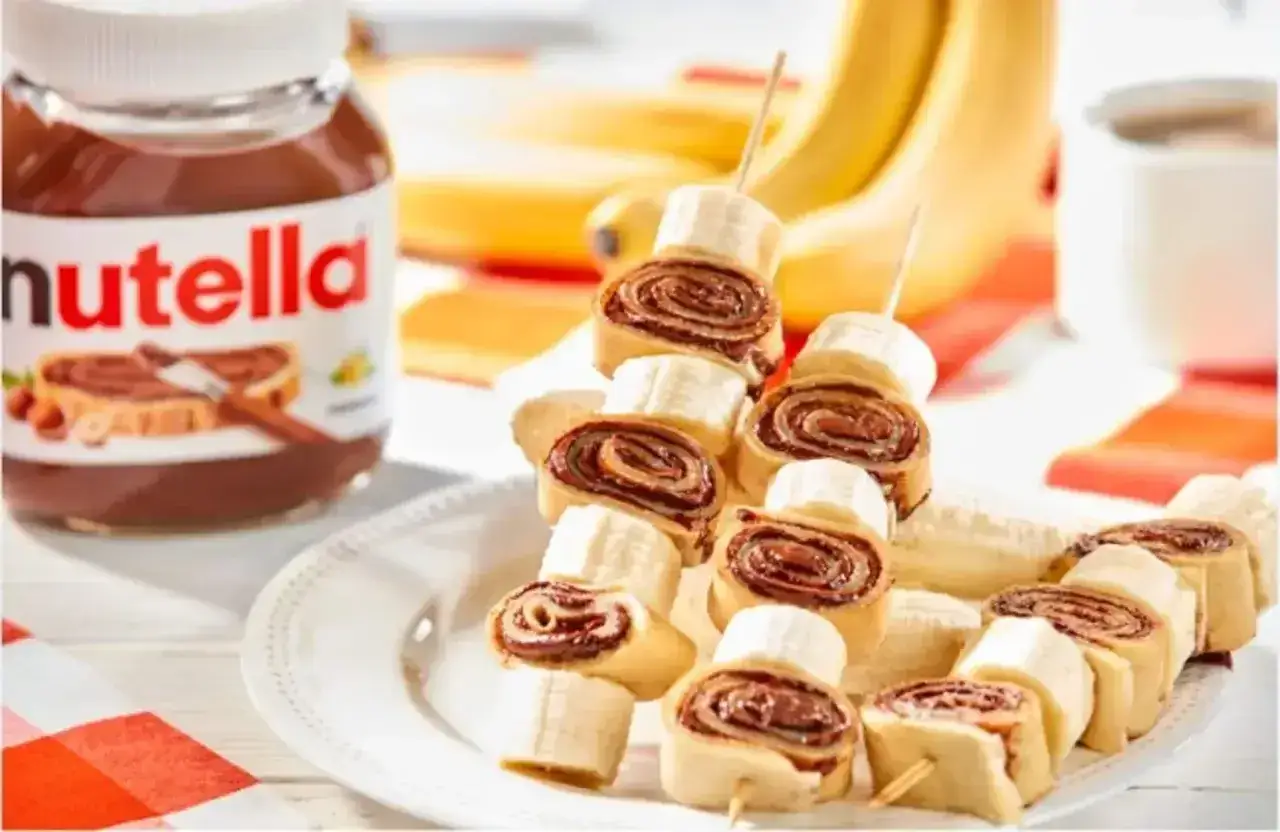 Naleśniki z nutellą i bananem na patyczkach, obok słoik nutelli i banany. Pyszna przekąska!