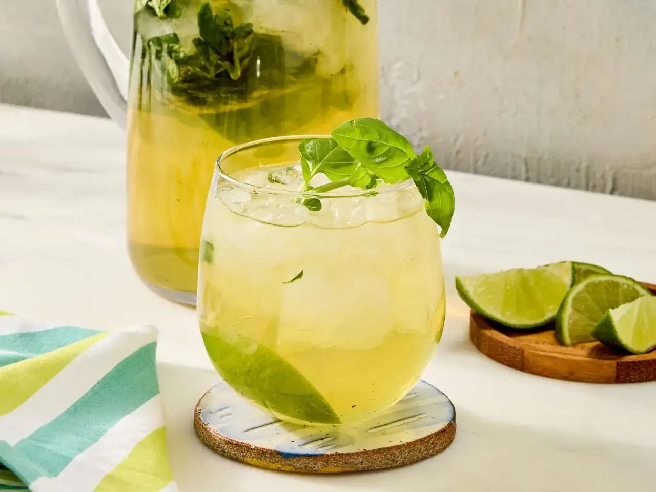 Orzeźwiający limoncello spritz z lodem, miętą i limonką, podany w szklance obok dzbanka z tym samym napojem.