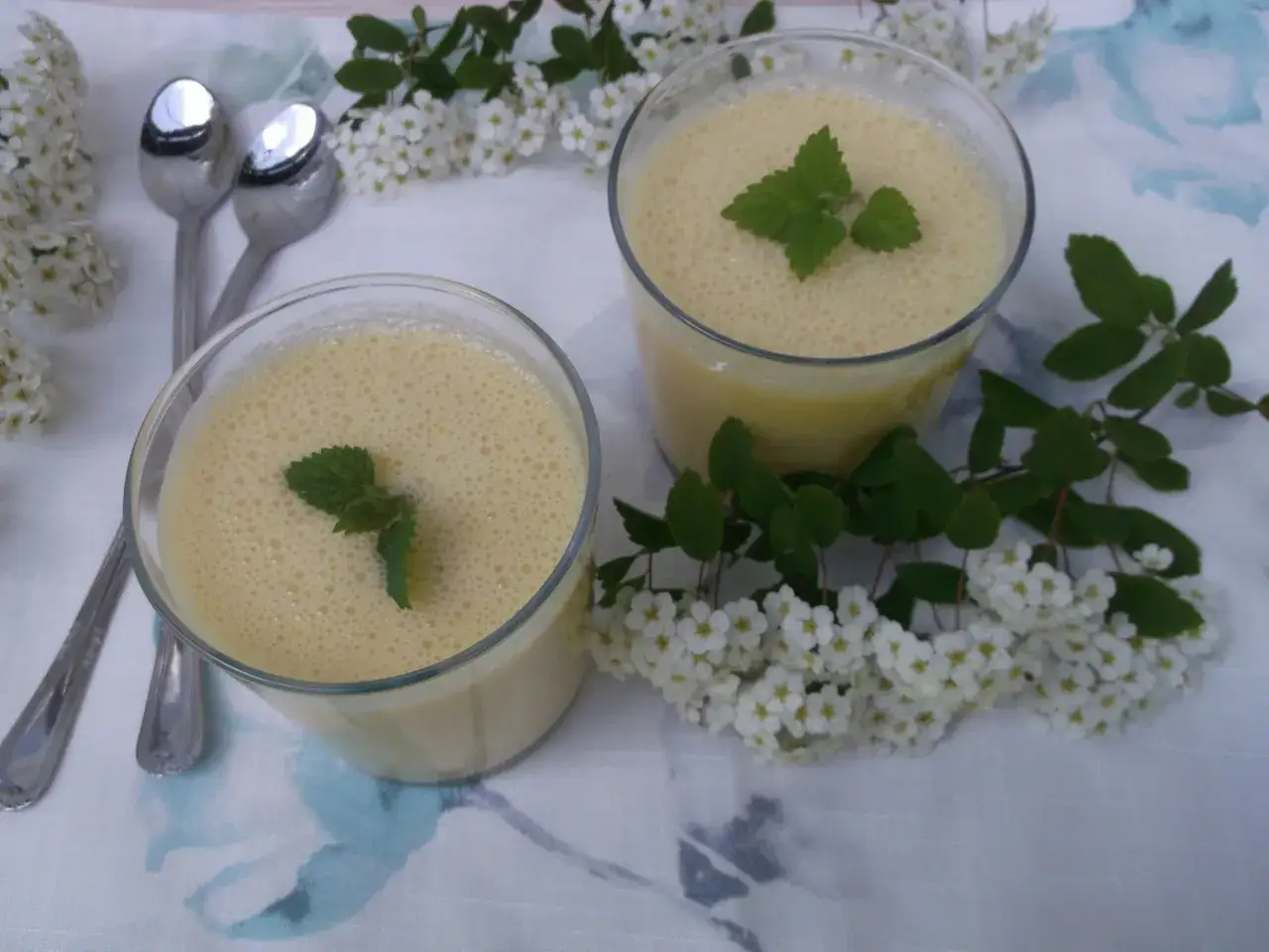 Dwa szklanki orzeźwiającego mango lassi, ozdobione listkami mięty, na tle kwitnących gałązek.