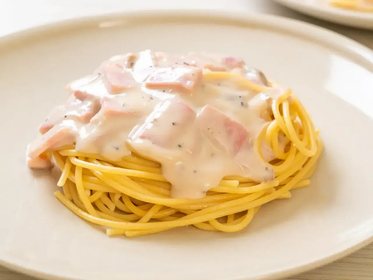 Spaghetti z kremowym sosem śmietanowym i kawałkami szynki, posypane pieprzem. Pyszny sos śmietanowy do makaronu.