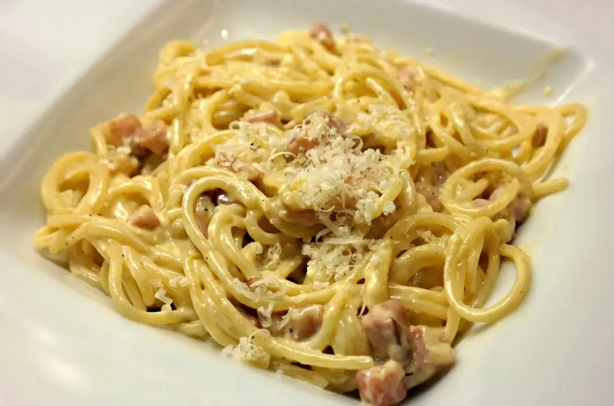 Pyszne spaghetti carbonara ze śmietaną bez jajek, posypane parmezanem i kawałkami boczku.