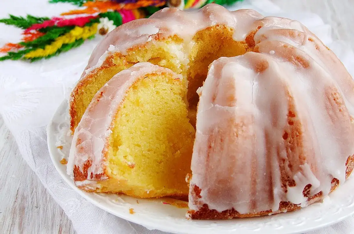 Najbardziej wilgotna babka z lukrem, z wyciętym kawałkiem, prezentuje swoje puszyste wnętrze. W tle kolorowe palemki.